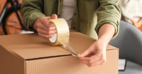 person taping a cardboard box shut with clear packing tape