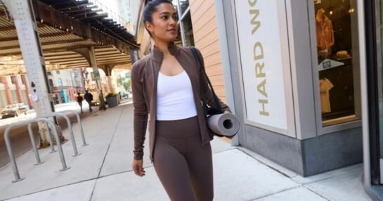 woman wearing Calia athletic clothing and carrying a yoga mat while walking on a sidewalk